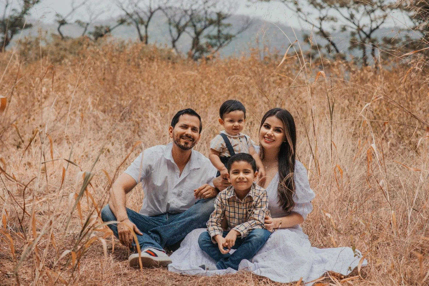 familia de cuatro sentada entre pastos altos y dorados durante una sesión de fotos familiar al aire libre